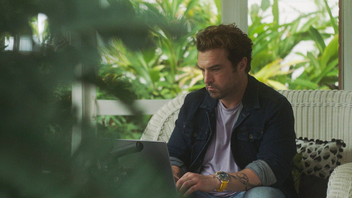 Collier Landry wearing a blue jacket and a white shirt sitting in front of a laptop outdoors.