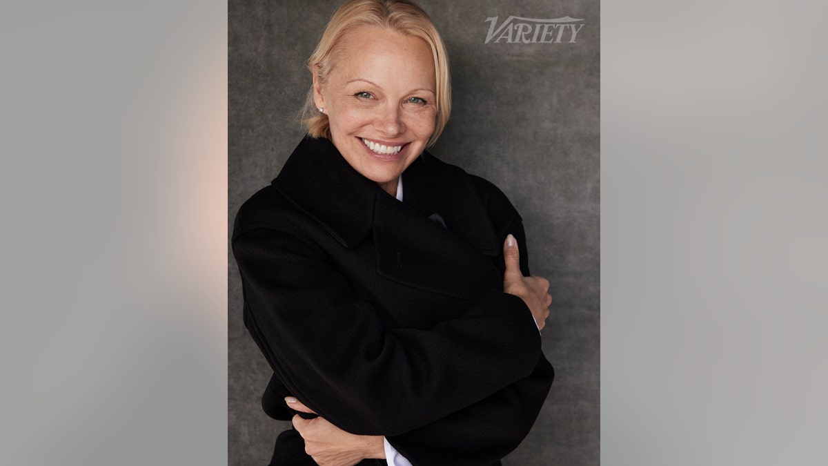 Pamela Anderson smiling in a black jacket sans makeup 