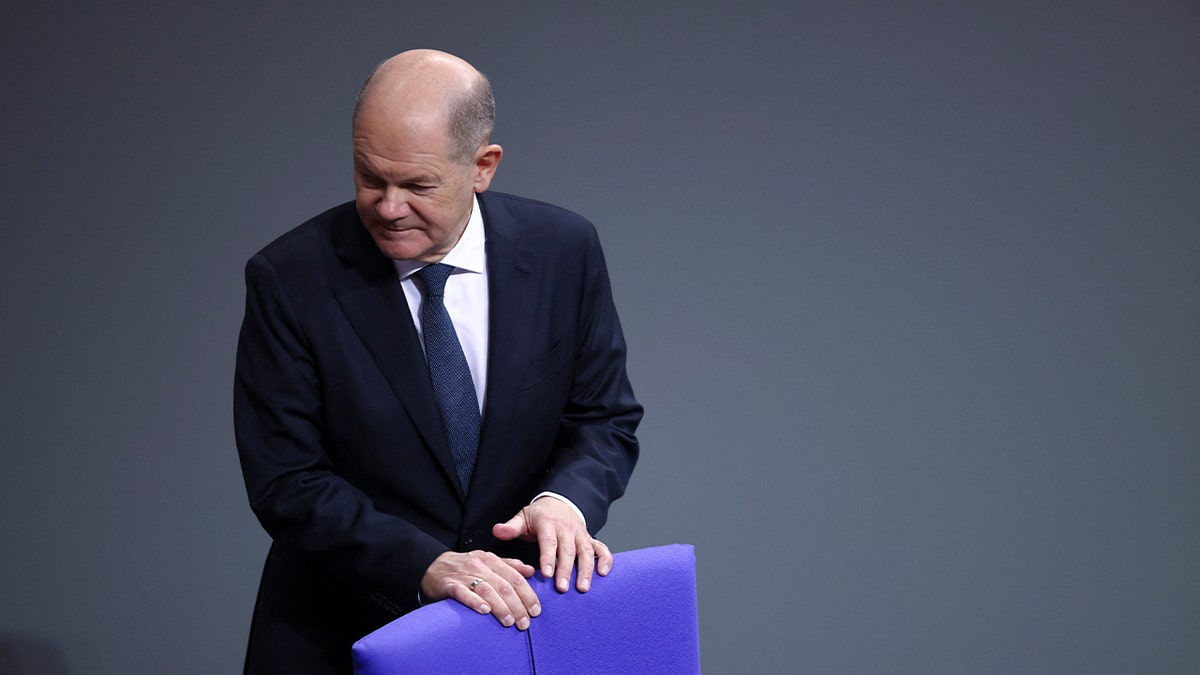 German Chancellor Olaf Scholz stands behind chair