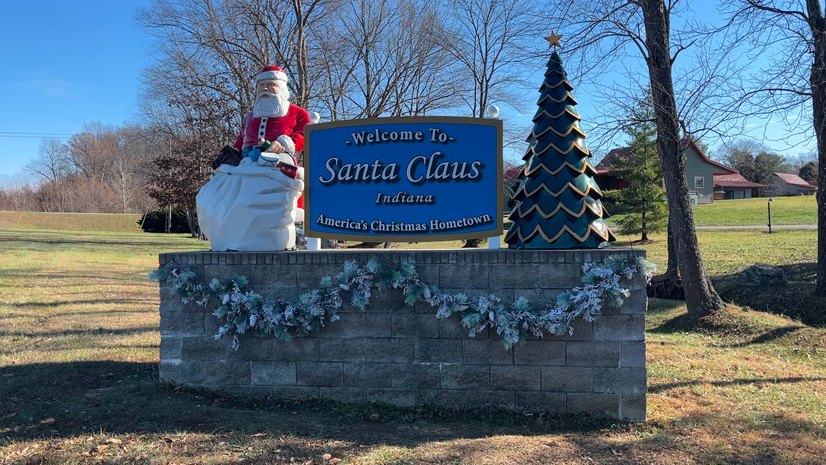 A festive welcome sign for Santa Claus, Indiana, featuring a Santa statue and a decorative Christmas tree.