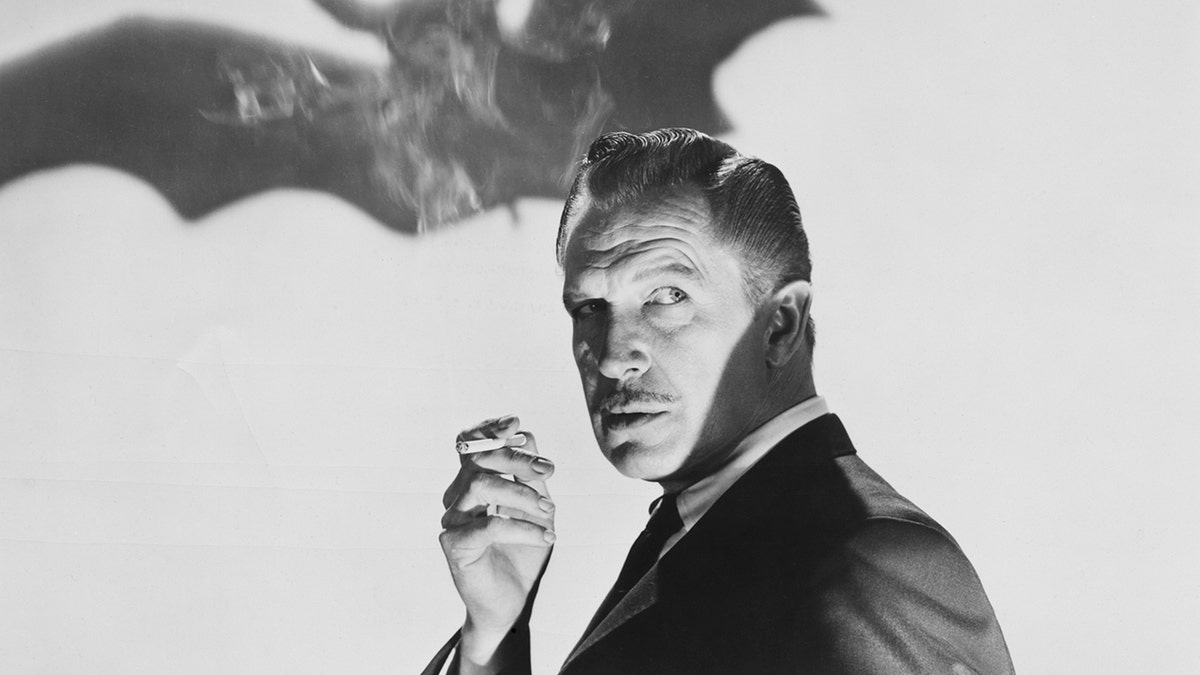 Vincent Price standing in front of a photo of a bat