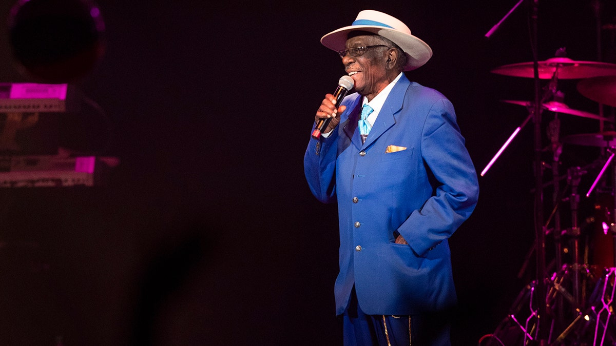 Brenton Wood wearing a blue suit and singing on stage