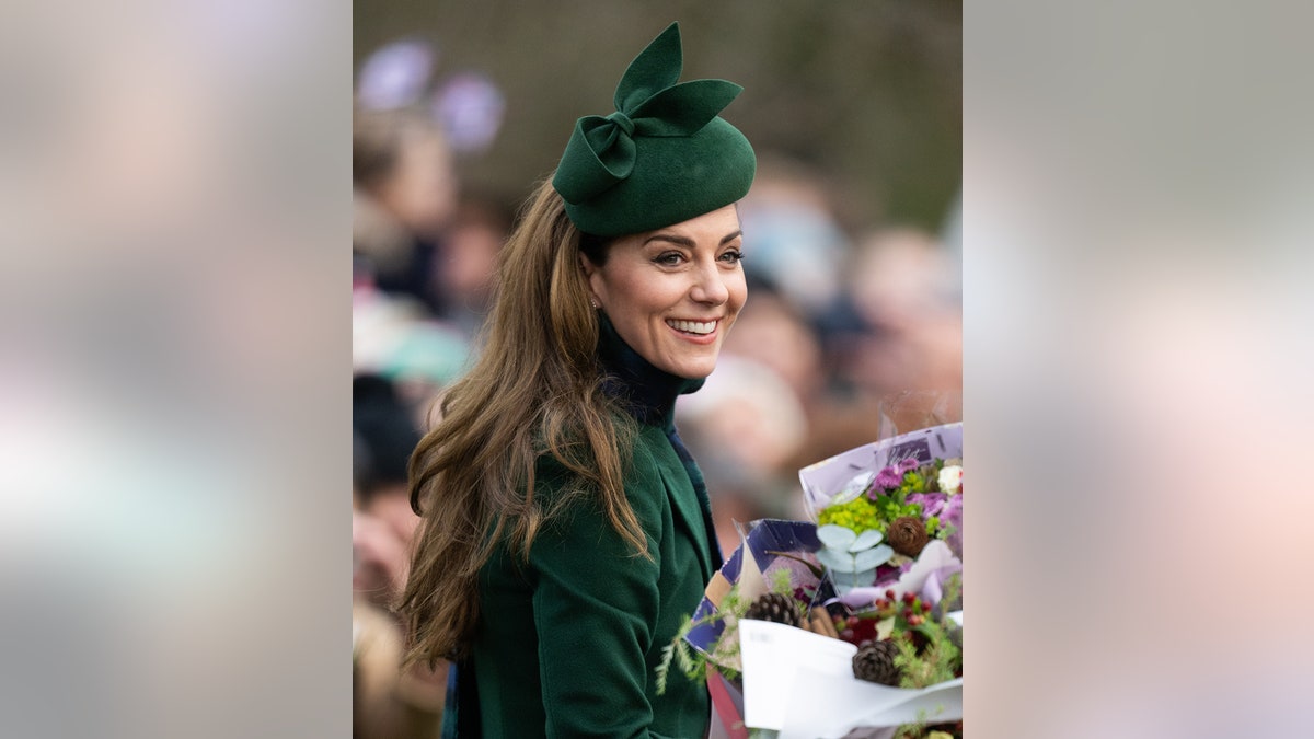 Kate Middleton smiling in a green coat and matching hat accepting a bouquet of flowers.