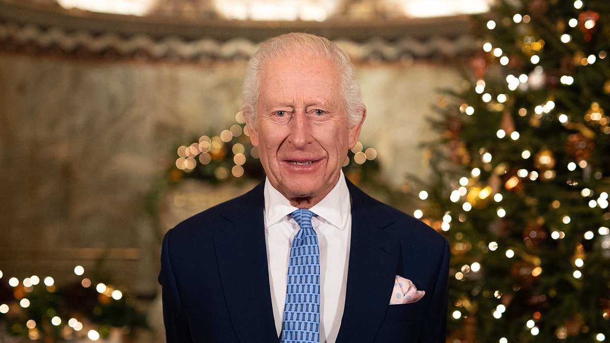 King Charles smiling next to a Christmas tree