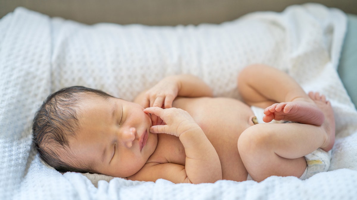 A newborn baby lays in her diaper in a cradle