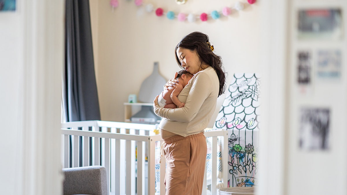 A new Mother stands in her daughters nursery holding her baby