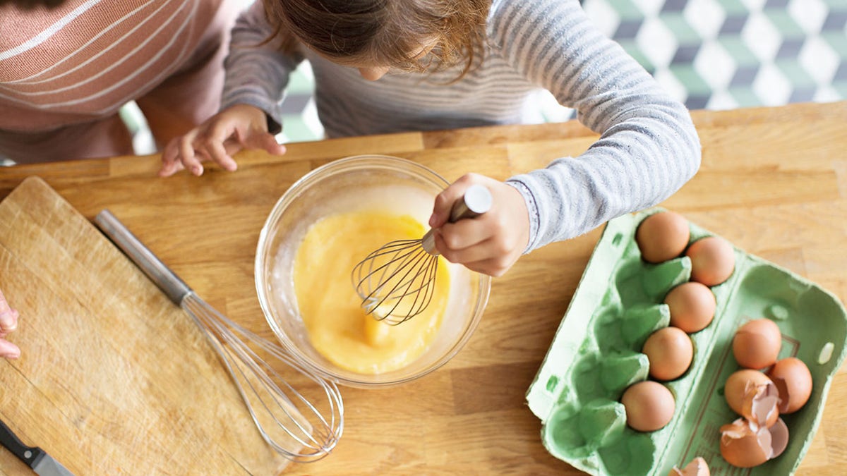 young girl whipping eggs in a bowl with a wire whisk in kitchen