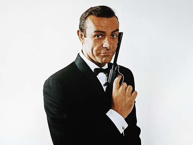 (Original Caption) Waist-up portrait of Sean Connery, as James Bond, caressing the barrel