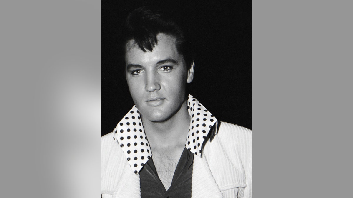 A close-up of Elvis Presley wearing a white blazer with a polka dot collared shirt.