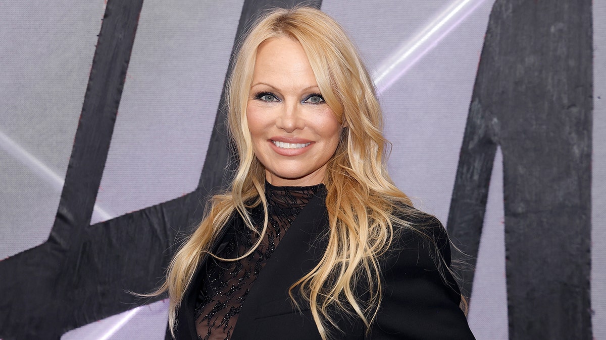 Pamela Anderson in a lace black top and black blazer smiles on the carpet