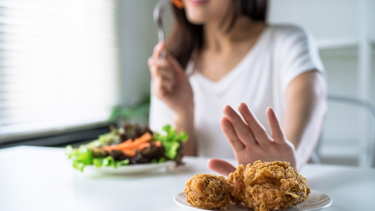 A woman eats salad and pushes away a plate of fried chicken.